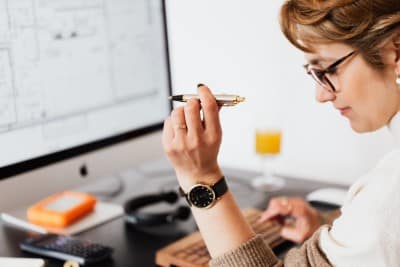Woman at work in front of a monitor holding a pen balancing and reconciling information